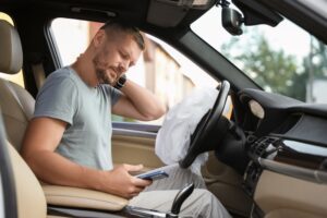 Man sitting in the driver’s seat of a car while holding his neck in pain as he wonders what he should do after a Denver car accident.
